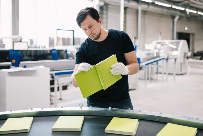 Mitarbeiter prüft Qualität der gedruckten Bücher in der Buchfertigungslinie bei der Buchbinderei optimal media